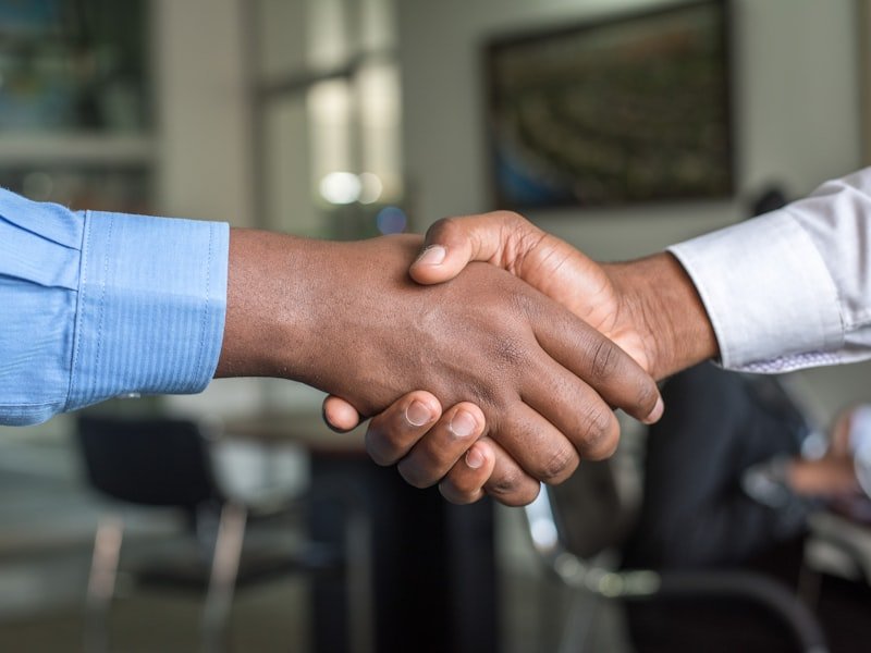 Two people shaking hands across a desk during an advisory meeting