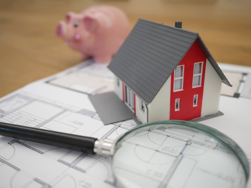 Model house with a magnifying glass resting on architectural blueprints